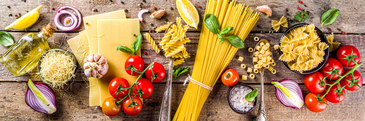 Assortment set of various raw pasta and condiments. Cooking italian pasta concept with fresh herbs and vegetables. Rustic style, wooden background top view copy space