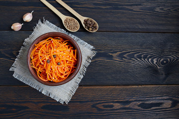 Wall Mural - Traditional Korean spicy carrot salad with garlic and coriander. Grated raw carrots in a ceramic bowl on a dark wooden background.