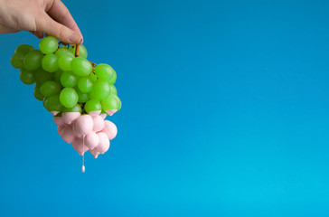 Paint dripping from green grapes on blue background