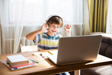 Child Boy In Headphones Is Using A Laptop And Study Online With Video Call Teacher At Home. Homeschooling, Distant Learning