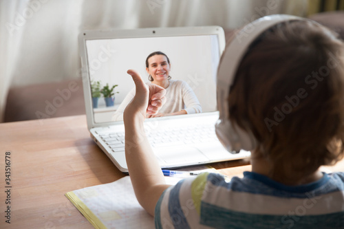Fotografía child boy in headphones show sight thumbs up, is using a laptop and Communicates with the teacher online at home