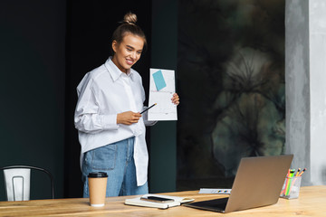 Business woman online meeting. Beautiful girl holds documents in her hand and communicates through web camera.