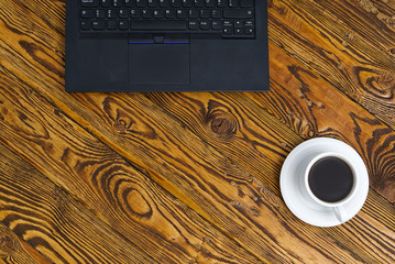 Poster - Laptop with cup of coffee on old brown wooden table. Top view to Notebook with cup of fresh coffee in home office in village.