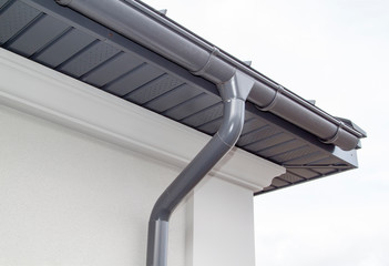 Corner of the house with new gray metal tile roof and rain gutter. Metallic Guttering System, Guttering & Drainage Pipe Exterior