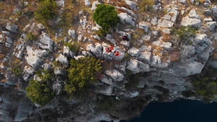 Sticker - A couple of tourists in love are sitting on the edge of a cliff overlooking the sea. Edge of the world. Peak. The end of hiking trail point. Destination. and an active lifestyle. Top down, rotation