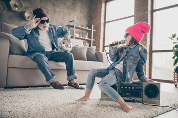 Photo of two people grandpa listen little granddaughter sing mic old fashion song cool style specs denim outfit hat house party sit tape player recorder stay home quarantine indoors