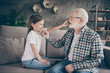 © deagreez - Profile photo of funny old grandpa little granddaughter sit sofa stay house quarantine safety playful good mood touch noses giggling modern interior living room indoors