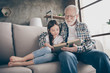 Photo of aged old grandpa little pretty granddaughter sit comfy sofa hugging stay house quarantine safety read interesting book fairy tale modern interior living room indoors