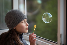 Girl Blowing Bubbles To Window At Home