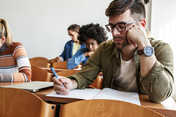 Wall Mural - In the university classroom, a portrait of a determined male student , absorbed in his test, showcasing his academic prowess and dedication to his studies.	