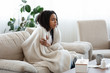© Prostock-studio - Sick black woman sitting on sofa covered with blanket, suffering from coronavirus