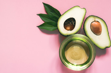 Two halves of avocado and avocado oil in a bowl on a pink background. Beauty theme. Skin care concept. Avocado with green leaves.