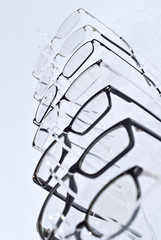 Poster - Many glasses on a white background. Glasses are stacked in a row on a transparent shop window. Glass stand on gray table. Sale and exhibition of optics.