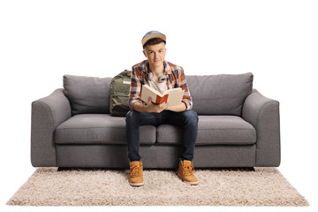 Poster - Male student sitting on a sofa holding a book and looking at the camera