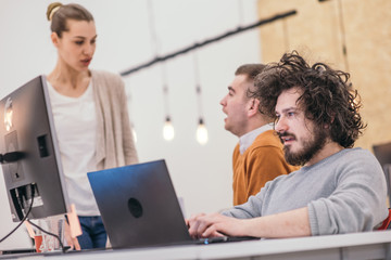 Coworkers, employees working and discussing a project they are preparing while typing on a laptop and looking at pc, computer.