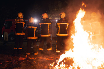 Wall Mural - Team of professional firefighters in front of a fire with firetruck in the background.