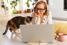 Woman Freelancer Lies On Carpet In Living Room, Watch Webinar. Female With Her Cat Talking Through Video Chat With Her Family Who Are In Isolation During The Coronavirus. Quarantine Life, Remote Work.