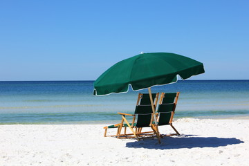 Two chairs and green umbrella on white sand beach