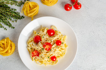 Homemade fettuccine pasta with tomatoes, thyme, parmesan cheese in a white plate on a light background.