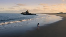 Aerial: Asian Woman Walking Along Beach At Sunset. Whatipu, Auckland, New Zealand