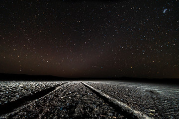 Wall Mural - a view of a dirt road with the track imprint in the sand going to the milky way on a starry night at