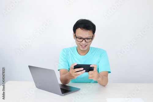 Cuadros en Lienzo Asian young man enjoy on the smartphone when play game at work