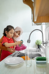 Wall Mural - asian muslim Daughter helping her mother in the kitchen washing dishes together