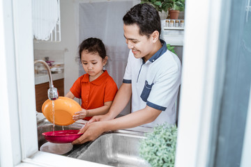 Wall Mural - Helping hand. Cute little Girl Help Her father In Washing Dishes At Family Kitchen