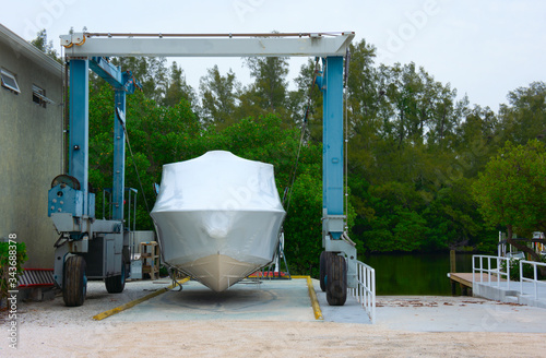Cuadros en Lienzo Shrink wrapped boat strapped on a mobile lift preparing it for winter storage, shipment or launching with a boat ramp and waterway canal in the background with many green trees