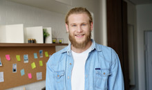 Positive Young Hipster Professional Man Student, Freelancer Standing At Home Office. Young Confident Smiling Adult Caucasian Bearded Casual Guy Looking At Camera. Head Shot Close Up Portrait.