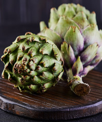 Wall Mural - Fresh artichokes on a wooden stand against a dark background