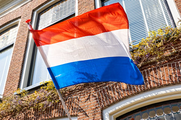 A dutch flag waving in the wind on the facade of a typical dutch house on Koningsdag. A national holiday in the Kingdom of the Netherlands