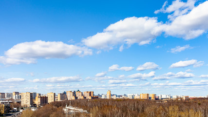 Canvas Print - blue sky with white cumulus clouds over city street and park on sunny March day