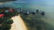 Aerial Ascending Footage Of Houses On Stilts Over Mossy Sea Water And White Beach, Batangas, Philippines.