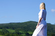 Young woman in a white dress in the background of a green hills and a blue sky