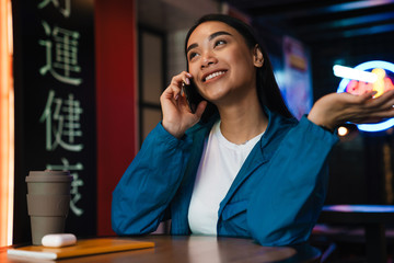 Poster - Photo of happy asian woman talking on mobile phone and smiling in cafe