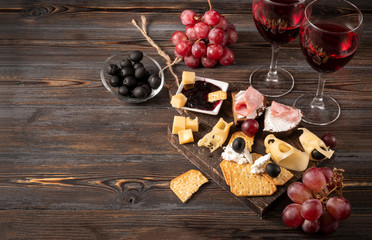 Wall Mural - cheese, cracker, ham, jam, grapes, olives, 2 glasses of red wine on a dark wooden background, appetizer, tapas