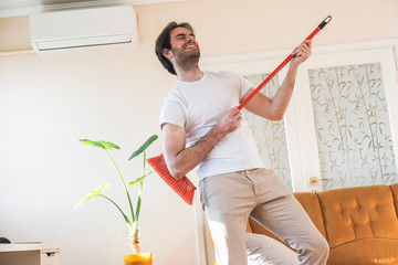 Wall Mural - Handsome man cleaning his house with broomstick and singing and feel happy