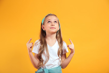 happy little girl pointing upwards at copy space on yellow background