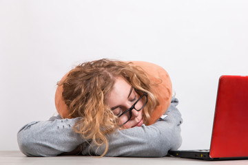 The girl works at the computer with pillow around her neck, on a white background. The concept of working from home, a sleepy lazy worker.