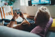 Young man relaxing at home lying on sofa with pet playing video games, man holding simulator joypad lying with dog on sofa, Home Leisure Concept