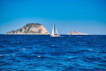 sailboat in the sea with two small rocky islands in the background