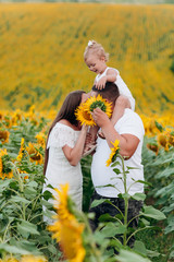 Wall Mural - Daddy's carrying a baby daughter on his shoulders in the field of sunflowers. The concept of summer holiday. Father's, mother's, baby's day. Spending time together. Family look. Couple kissing.