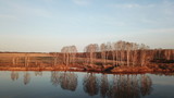 Fototapeta Zachód słońca - Frosty dry shore grass above calm river water reflecting blue morning sky, naked autumn trees