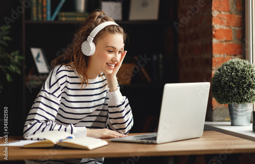 Excited woman in headphones having conversation on video chat while using laptop at home Tableau sur Toile
