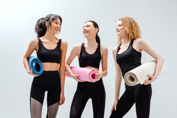 Wall Mural - happy and multicultural women holding fitness mats on white