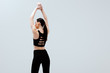 © LIGHTFIELD STUDIOS - woman in black sportswear standing with hands above head isolated on white