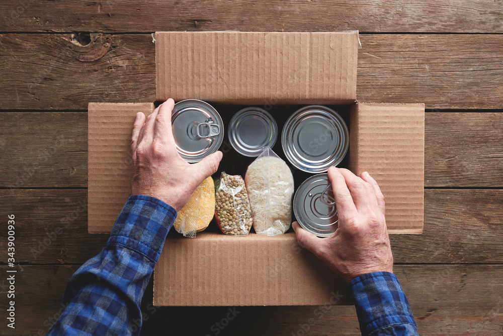 a person packing a donation box with food items - obrazy, fototapety, plakaty 