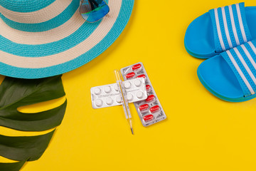 Wall Mural - Top view on thermometer, white and red pills in blister pack, blue hat, blue flip-flops, sunglasses, monstera leaf on yellow background. Concept of beach holiday, sea tour, warm sunny summer