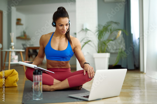 Young muscular build woman following online exercises class over laptop at home.